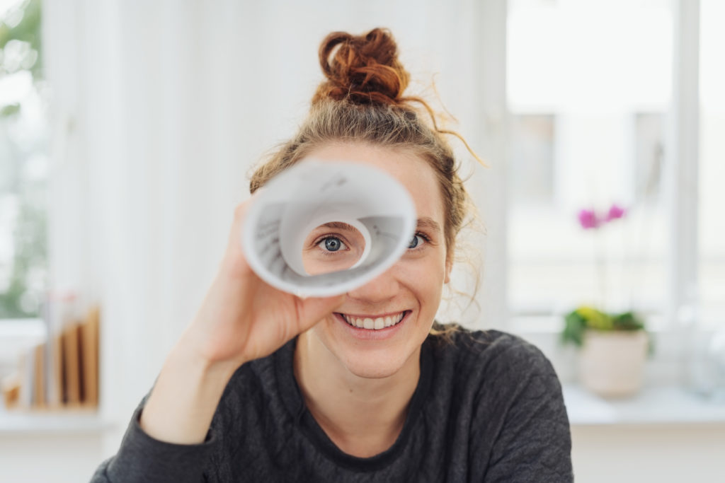 Frau schaut durch ein aufgerolltes Blatt